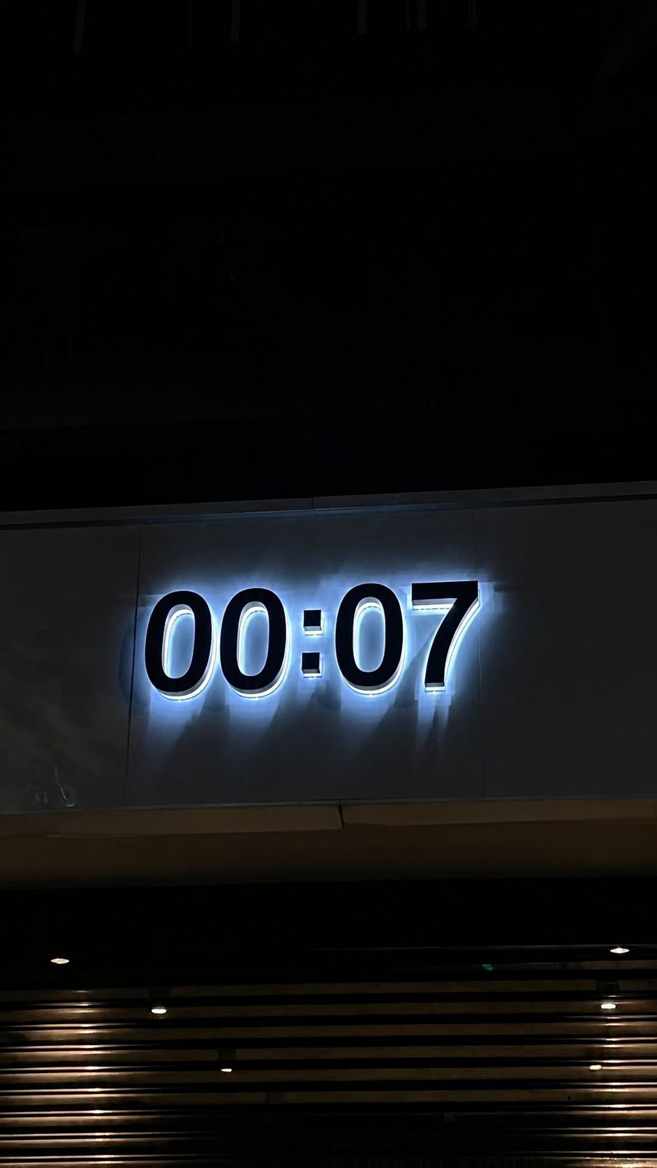 Letreiro iluminado 00:07 numa fachada à noite